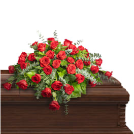 Red rose casket spray with greenery on a wooden casket