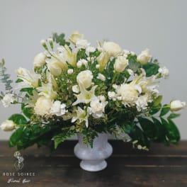 White floral arrangement in a white vase with roses and lilies