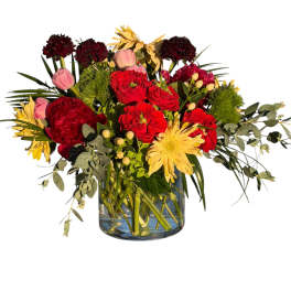 Red and pink flowers in a glass vase with yellow blooms