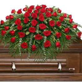Red rose casket spray with greenery on a wooden casket