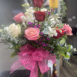 Mixed bouquet of red, pink, and white roses with accent flowers and a large pink polka-dot bow.