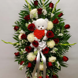 Standing floral spray with red roses, white blooms, and a teddy bear centerpiece