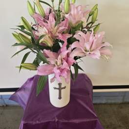 Pink lilies arranged in a white vase with a cross emblem