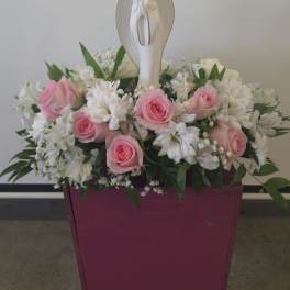 Pink roses and white flowers arranged around a white angel figurine in a magenta box