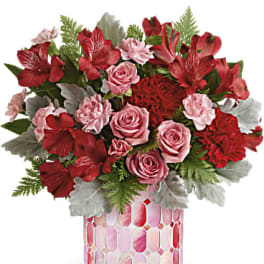 Red and pink floral arrangement in a pink mosaic vase