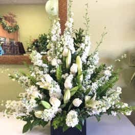 Large white floral arrangement with lilies and roses in a black container