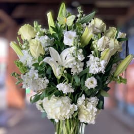 White lilies and pale roses in a tall glass vase