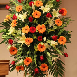 Large standing floral spray with red roses, orange gerberas, and white lilies