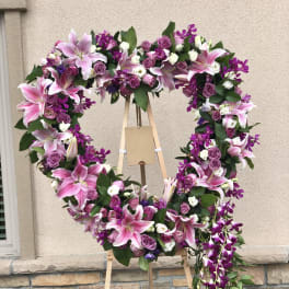 Heart-shaped floral wreath with pink lilies, purple roses, and orchids on an easel