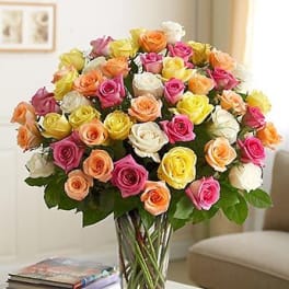 Mixed roses in pink, peach, yellow, and white in a clear glass vase