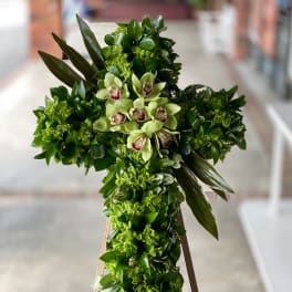 Green floral cross with pale orchids on a stand