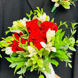 Red roses and white flowers in a hand-tied bouquet with green foliage