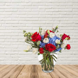 Bouquet of red roses, blue hydrangeas, and white blooms in a glass vase