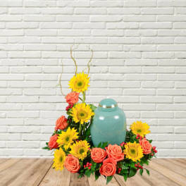 Coral roses and yellow sunflowers arranged around a teal urn.