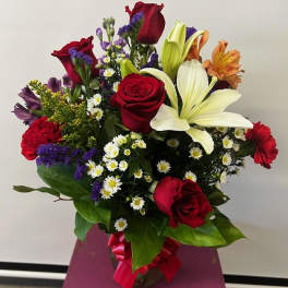 Mixed bouquet of red roses, white lilies, and purple filler flowers in a vase