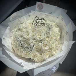 Bouquet of white roses wrapped in printed paper with a birthday topper