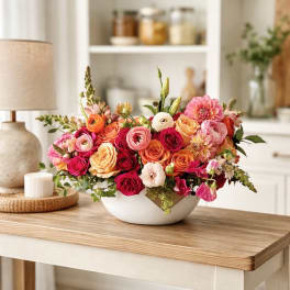 Mixed bouquet of pink, orange, and white flowers in a white bowl vase
