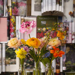 Three small glass vases hold colorful mixed flowers on a stone pedestal.