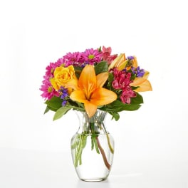 Mixed bouquet with yellow lilies, roses, and pink daisies in a clear glass vase
