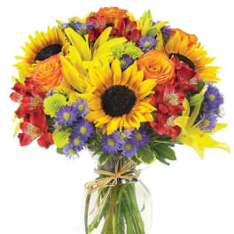 Bright mixed bouquet with sunflowers, roses, and purple daisies in a glass vase