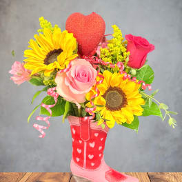 Bouquet of sunflowers and pink roses in a pink boot vase with a heart topper