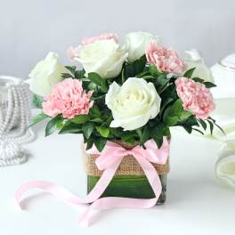 Pink carnations and white roses in a glass vase with a pink ribbon