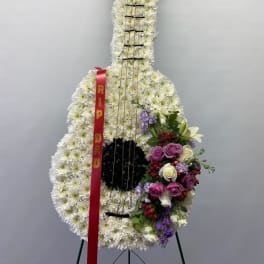 Standing guitar-shaped floral tribute with white flowers and a red ribbon