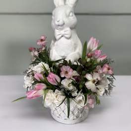 White bunny figurine in a flower basket with pink and white tulips