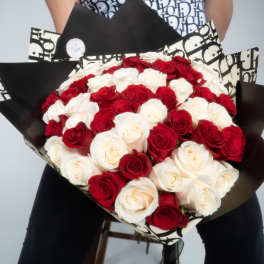 Large hand-tied bouquet of red and white roses wrapped in black and cream graphic paper.