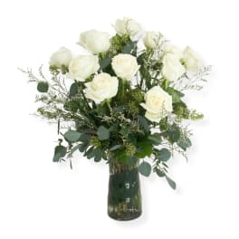 White roses arranged in a clear glass vase with airy greenery