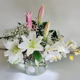 White lilies and pink buds arranged in a clear glass vase