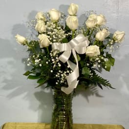 White roses arranged in a glass vase with a white ribbon