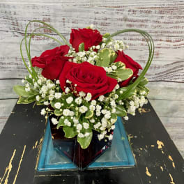 Red roses in a square glass vase with white filler flowers
