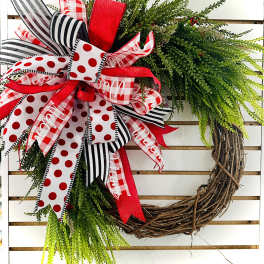 Decorative wreath with red, black, and white ribbons on a grapevine base