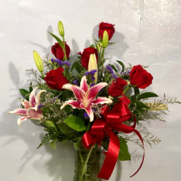 Bouquet of red roses and pink lilies in a glass vase with a red ribbon