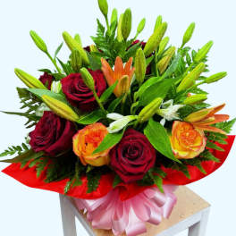 Bouquet of red and orange roses with lilies and a pink ribbon