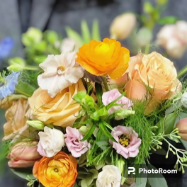 Handheld bouquet of peach roses, orange ranunculus, and pastel blooms against a dark jacket.