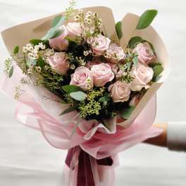 Bouquet of pale pink roses with small white filler flowers and pink wrapping
