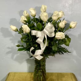 White roses arranged in a glass vase with a white ribbon
