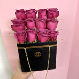 Pink roses arranged in a black handbag-style box with gold chain handles