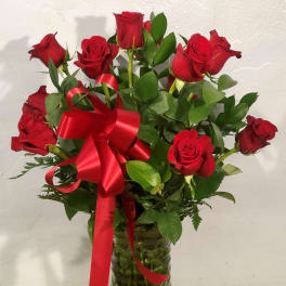 Red roses arranged in a clear glass vase with a red ribbon bow