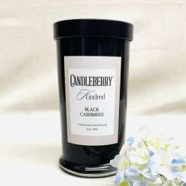 Black candle jar with a label beside pale blue and white flowers