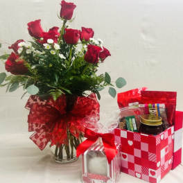 Red roses in a glass vase with a red ribbon, beside a Valentine gift basket
