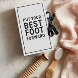 Gift box with a card reading "Put Your Best Foot Forward" and a pair of foot brushes