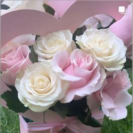 Pink and white roses in a pink heart-shaped box with a ribbon