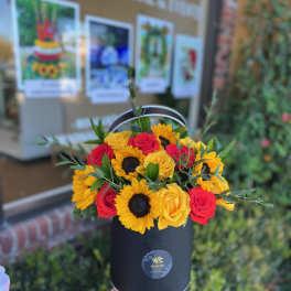 Bouquet of red and yellow roses with sunflowers in a black hat box