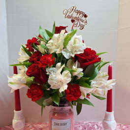 Red and white flower arrangement in a glass jar with a Valentine's Day topper