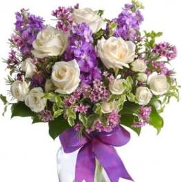 White roses and purple flowers arranged in a clear vase with a purple ribbon