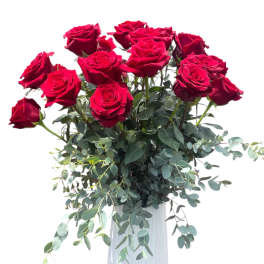 Red roses arranged in a white vase with trailing greenery