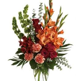 Tall mixed bouquet of orange, red, and peach flowers in a clear vase